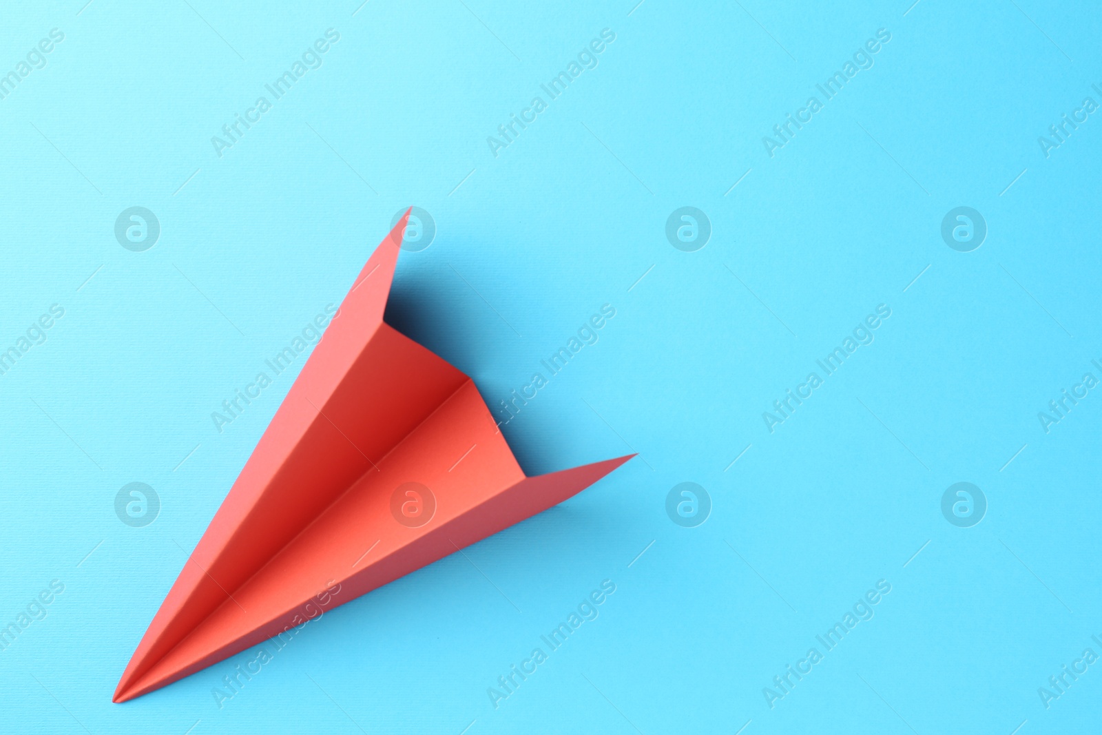 Photo of One handmade coral paper plane on light blue background, top view. Space for text