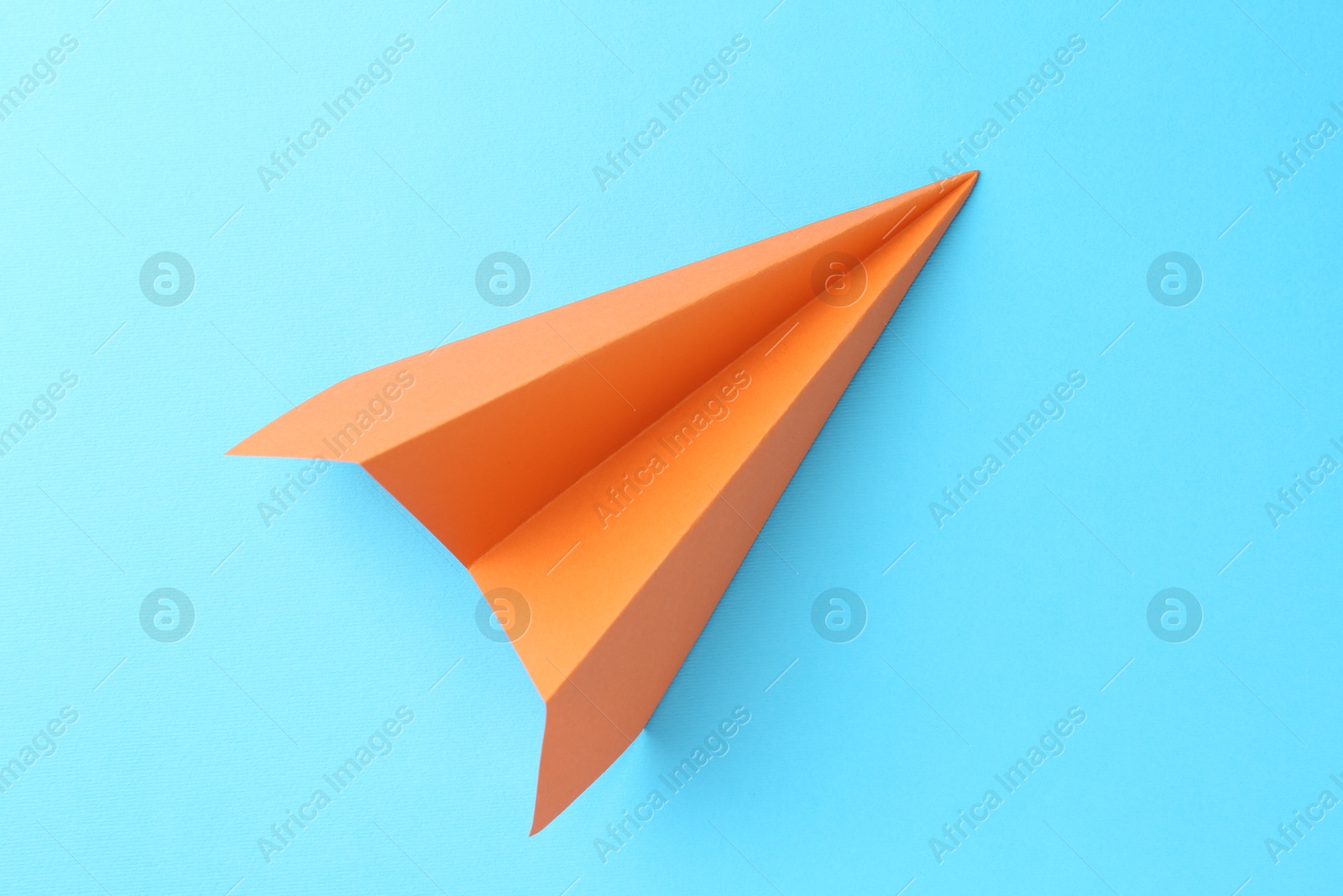 Photo of One handmade orange paper plane on light blue background, top view