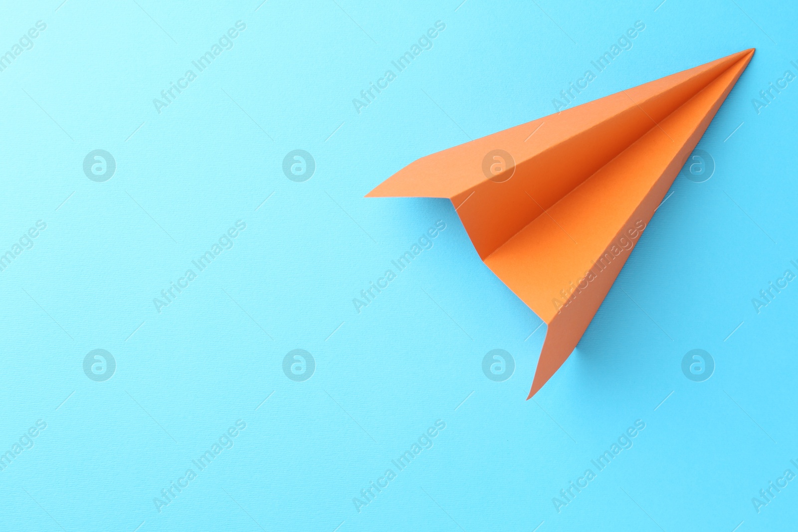 Photo of One handmade orange paper plane on light blue background, top view. Space for text