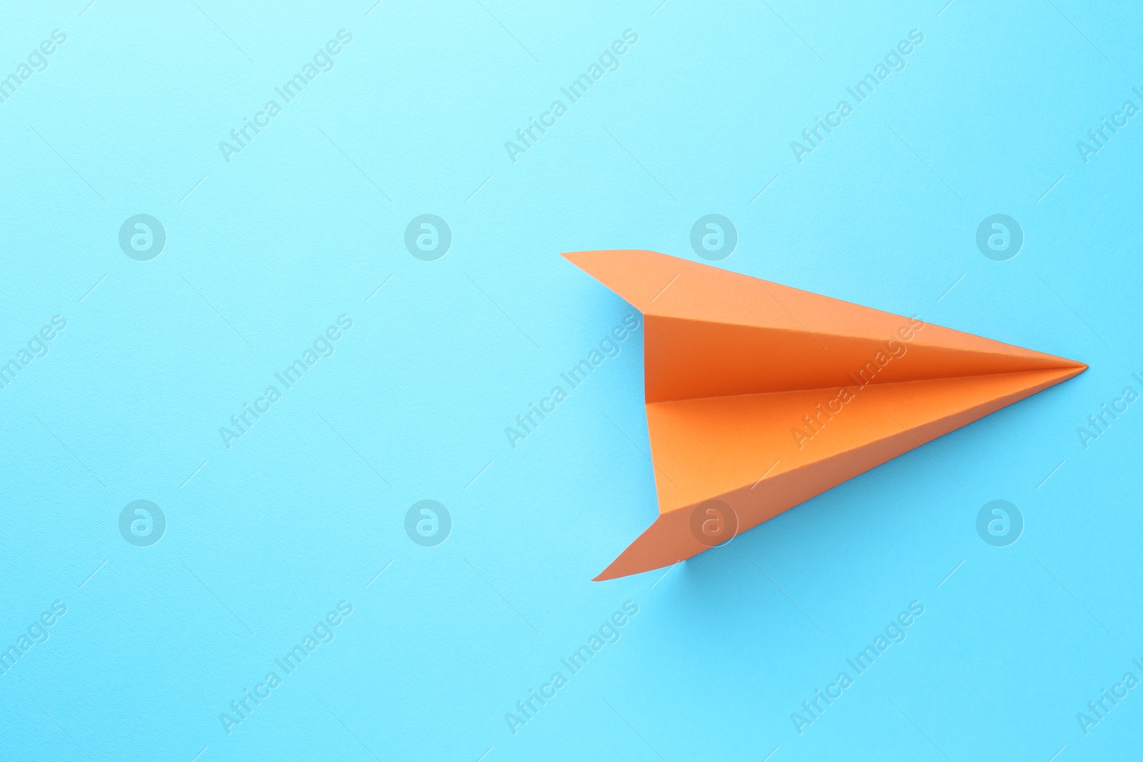 Photo of One handmade orange paper plane on light blue background, top view. Space for text