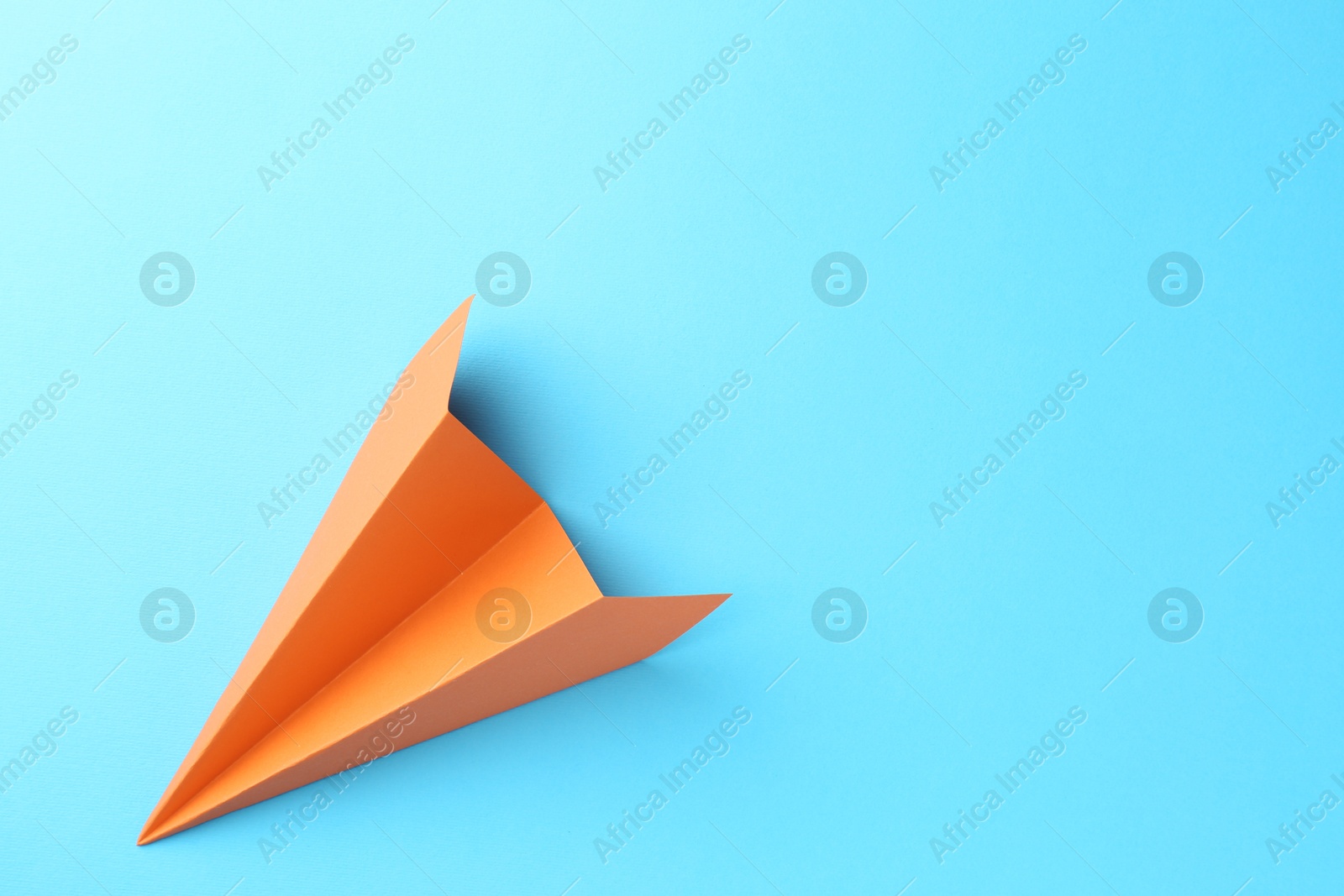 Photo of One handmade orange paper plane on light blue background, top view. Space for text