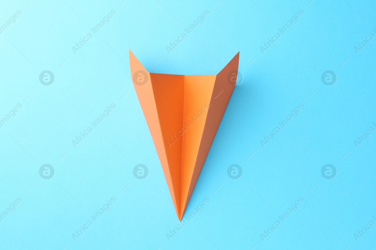 Photo of One handmade orange paper plane on light blue background, top view