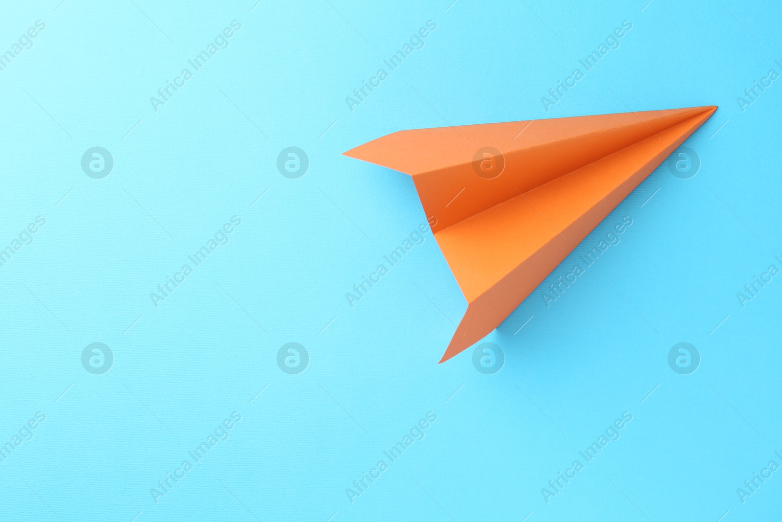 Photo of One handmade orange paper plane on light blue background, top view. Space for text