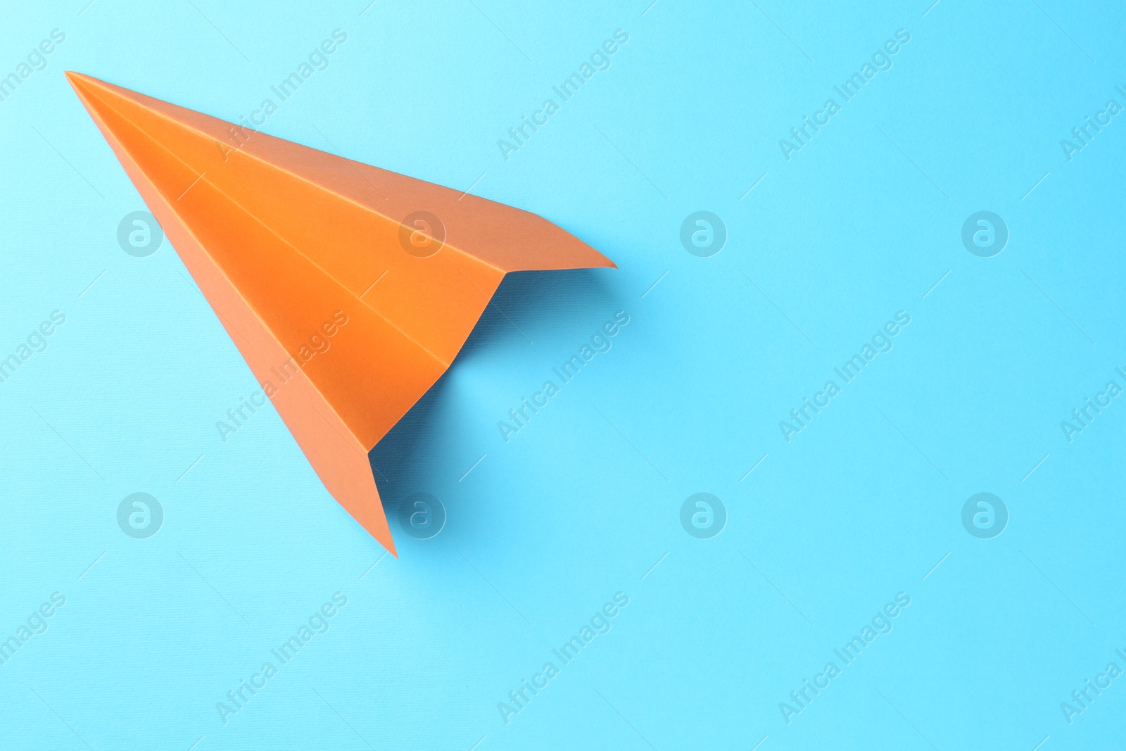 Photo of One handmade orange paper plane on light blue background, top view. Space for text