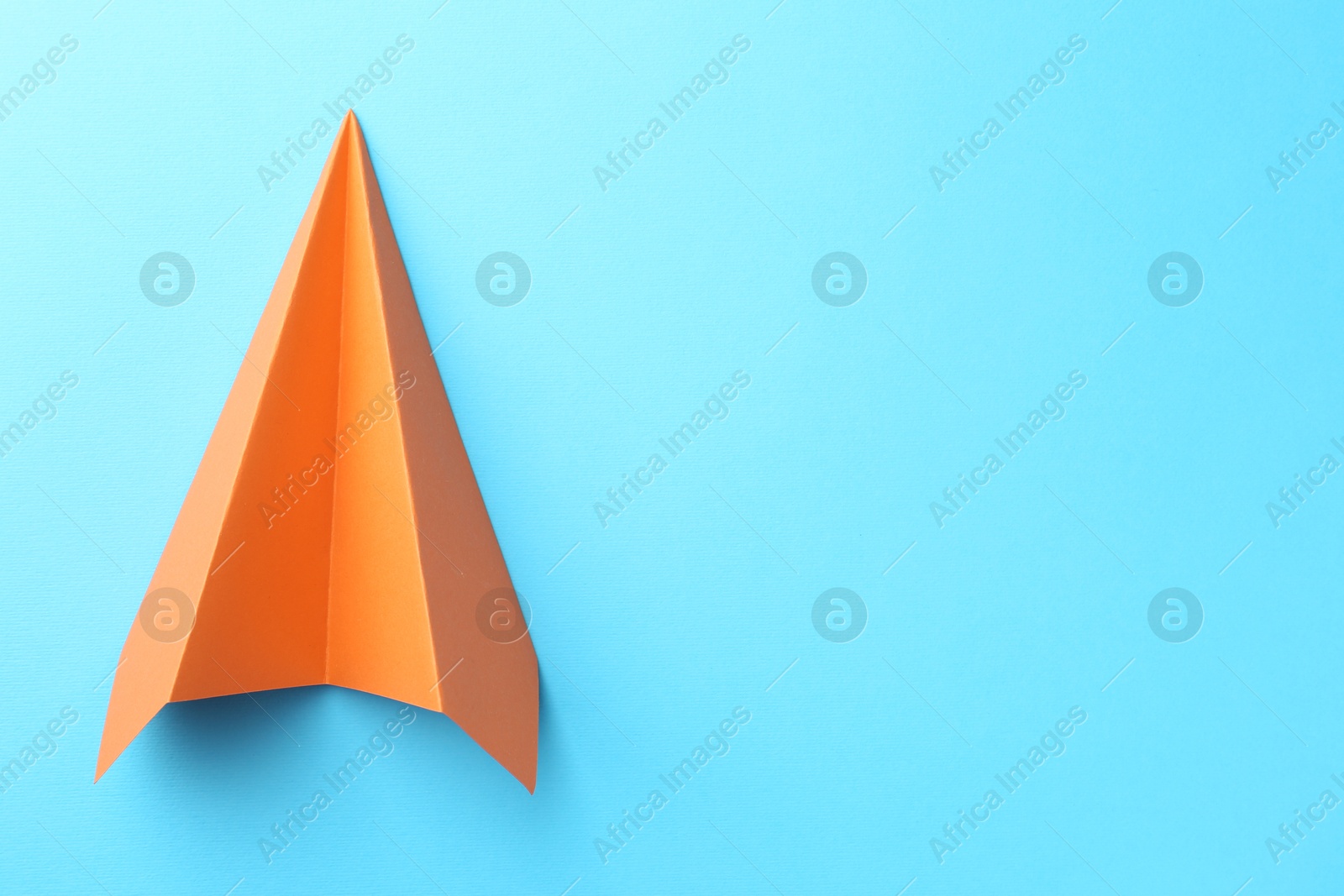 Photo of One handmade orange paper plane on light blue background, top view. Space for text