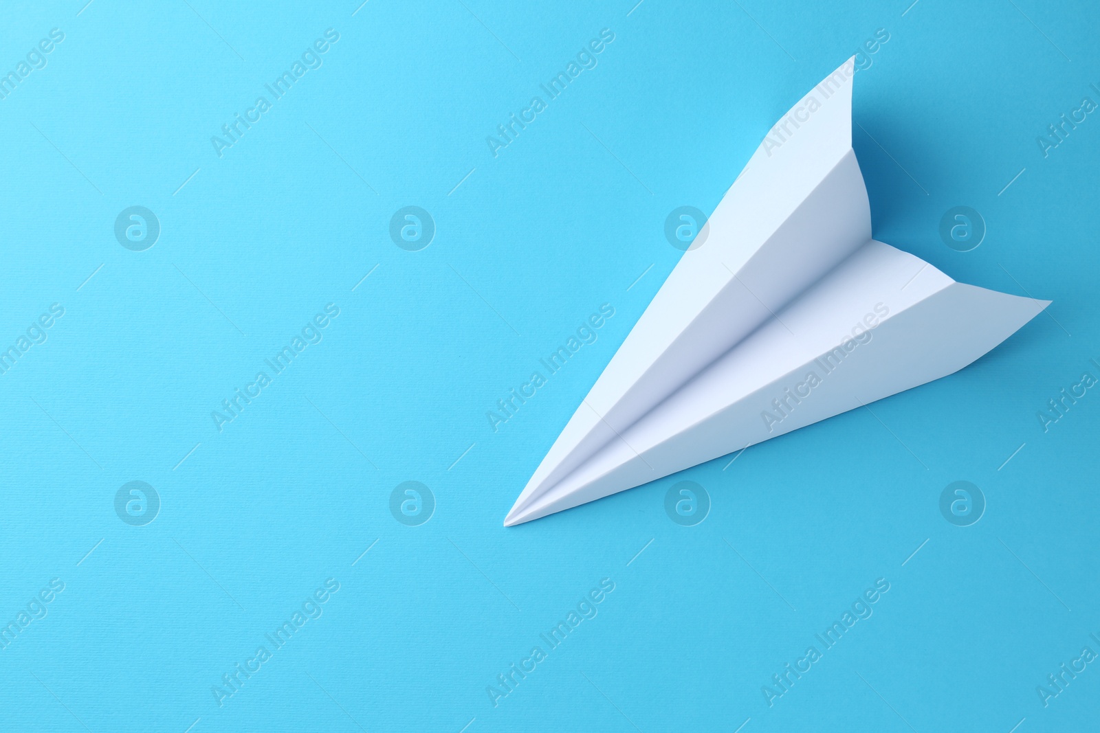 Photo of One handmade paper plane on light blue background, top view. Space for text