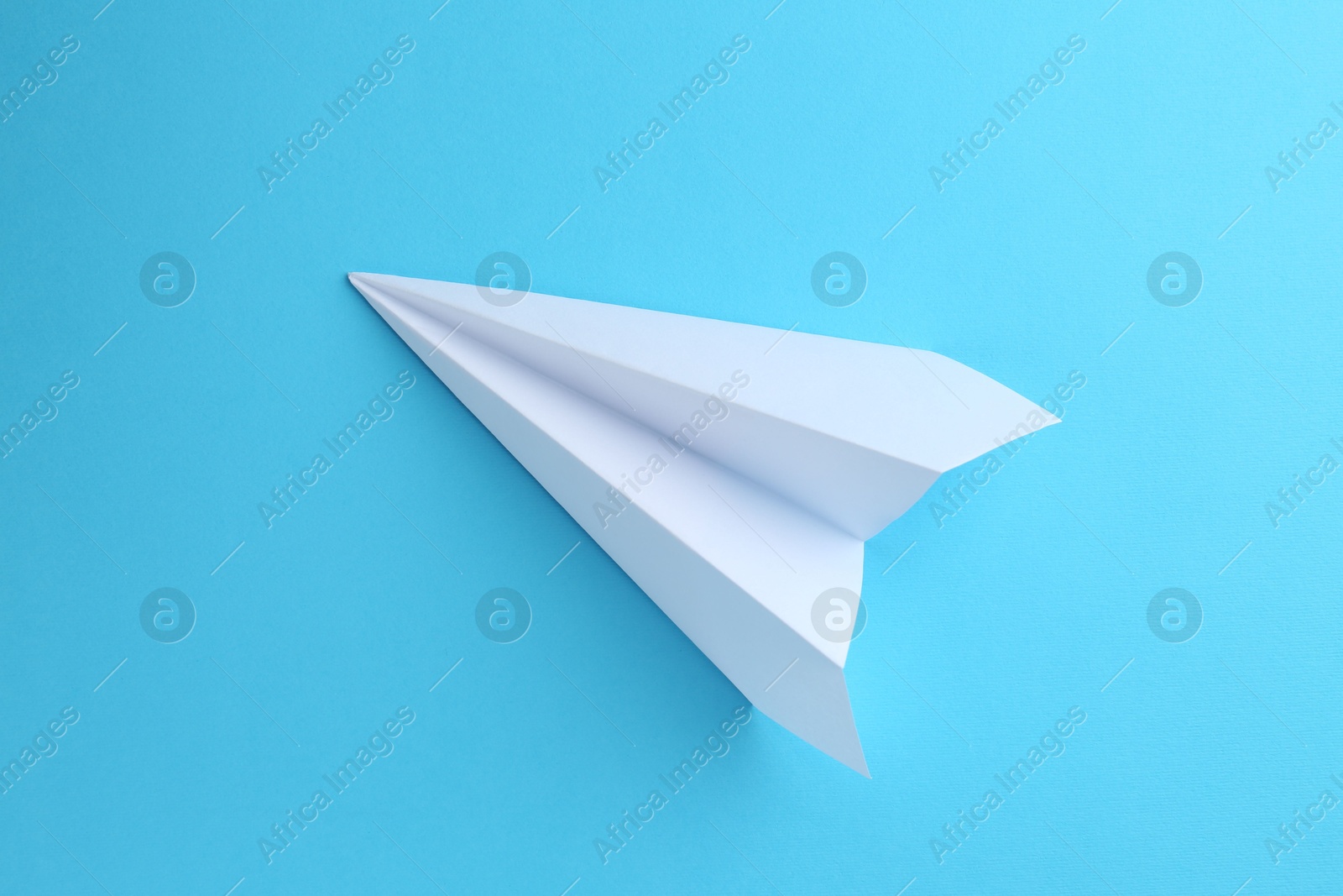 Photo of One handmade paper plane on light blue background, top view