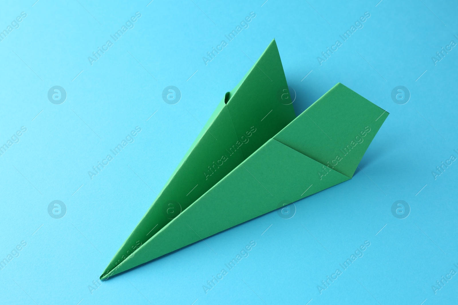 Photo of One handmade green paper plane on light blue background