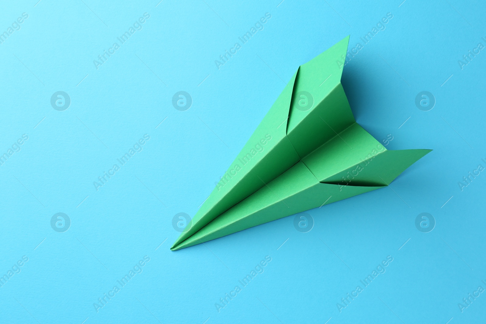 Photo of One handmade green paper plane on light blue background, top view. Space for text