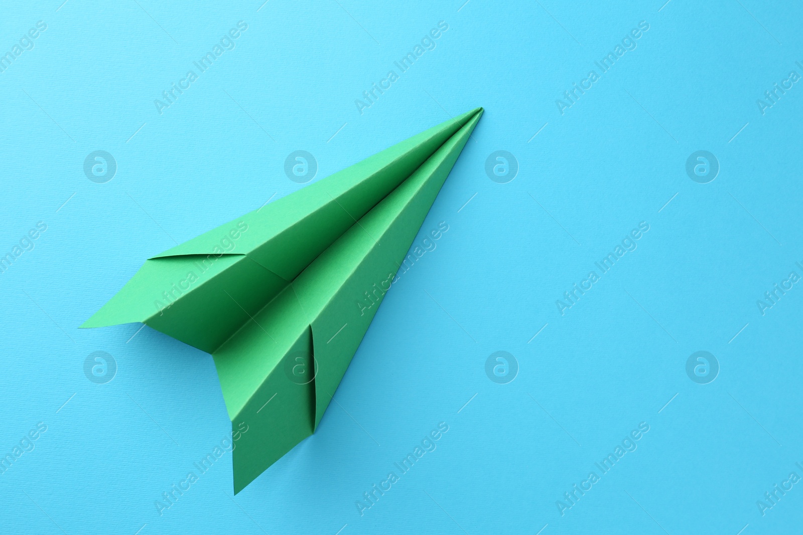 Photo of One handmade green paper plane on light blue background, top view. Space for text