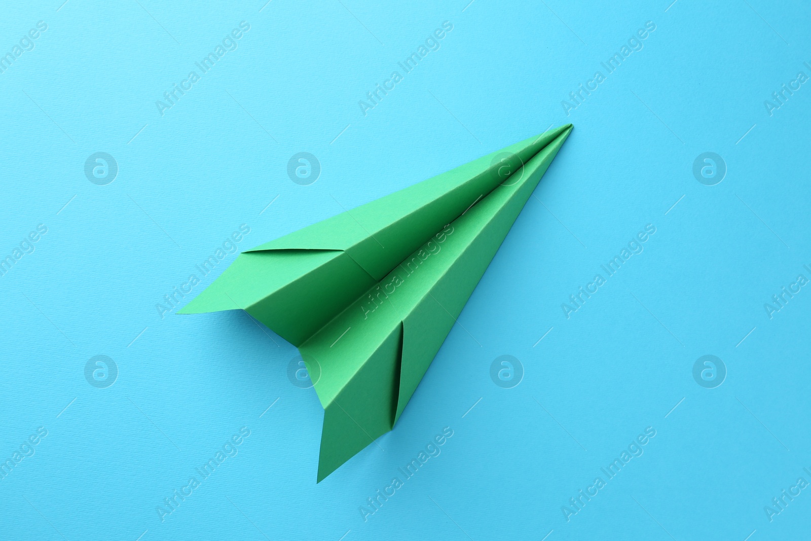 Photo of One handmade green paper plane on light blue background, top view