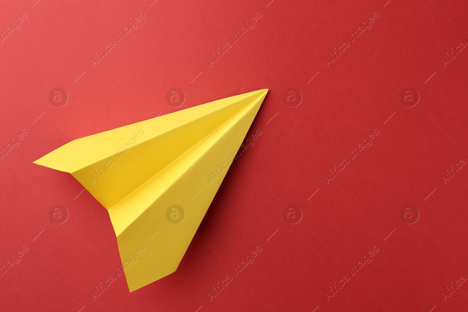 Photo of One handmade yellow paper plane on red background, top view. Space for text