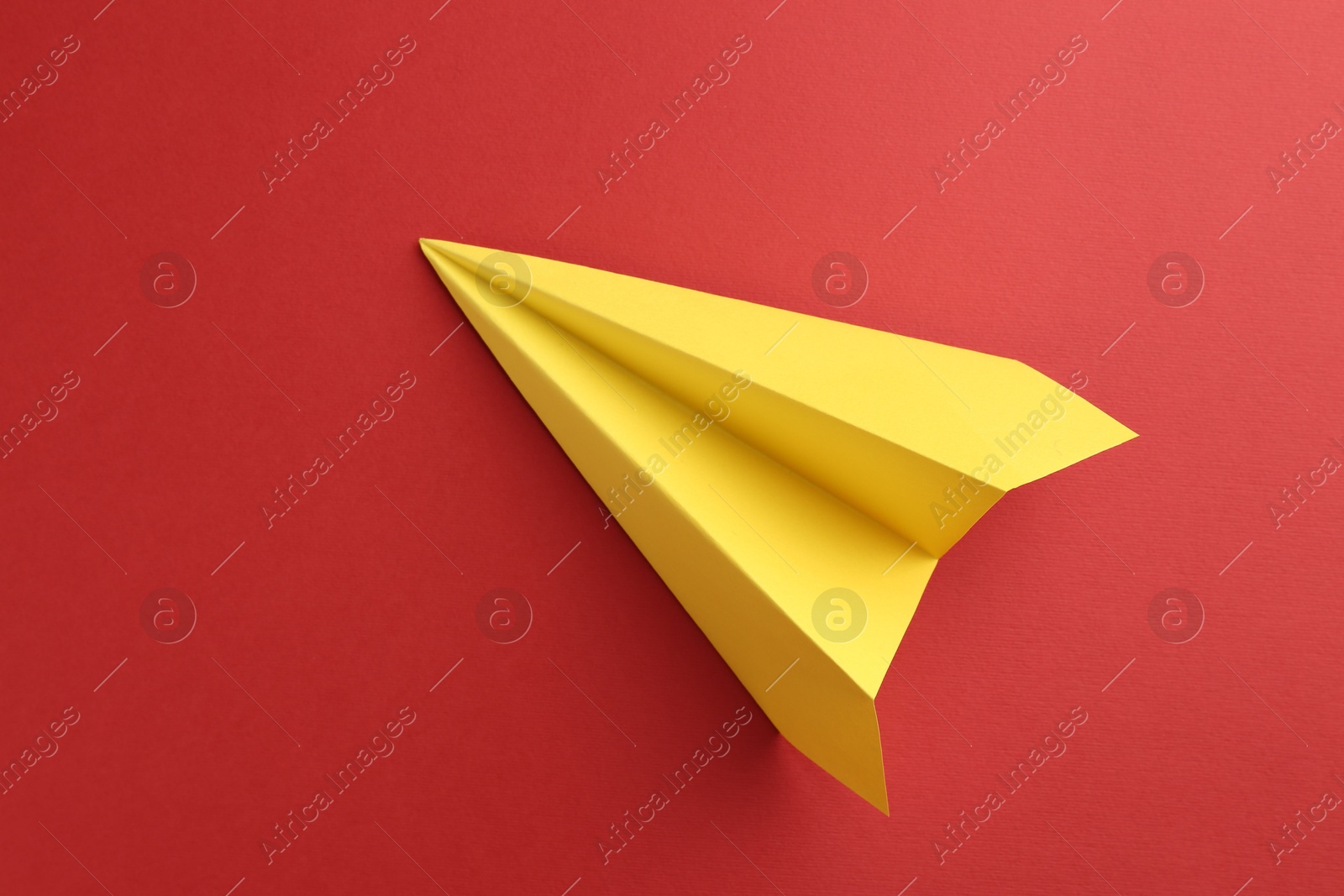 Photo of One handmade yellow paper plane on red background, top view