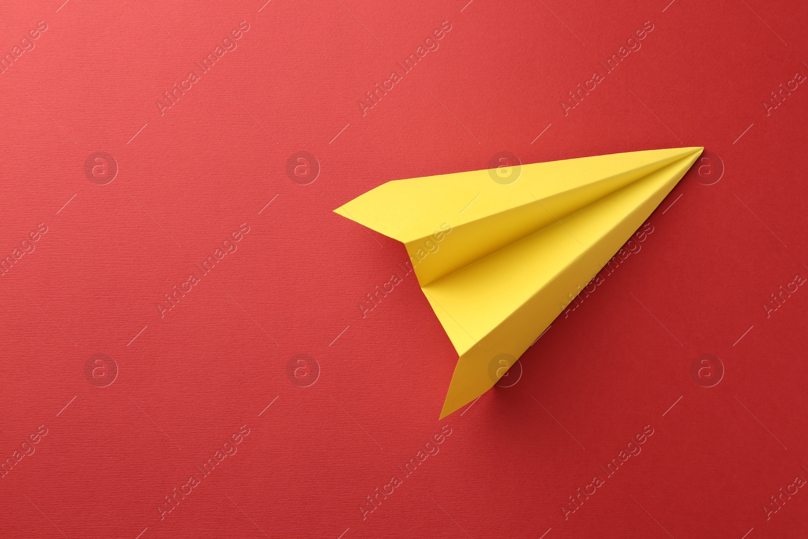 Photo of One handmade yellow paper plane on red background, top view. Space for text