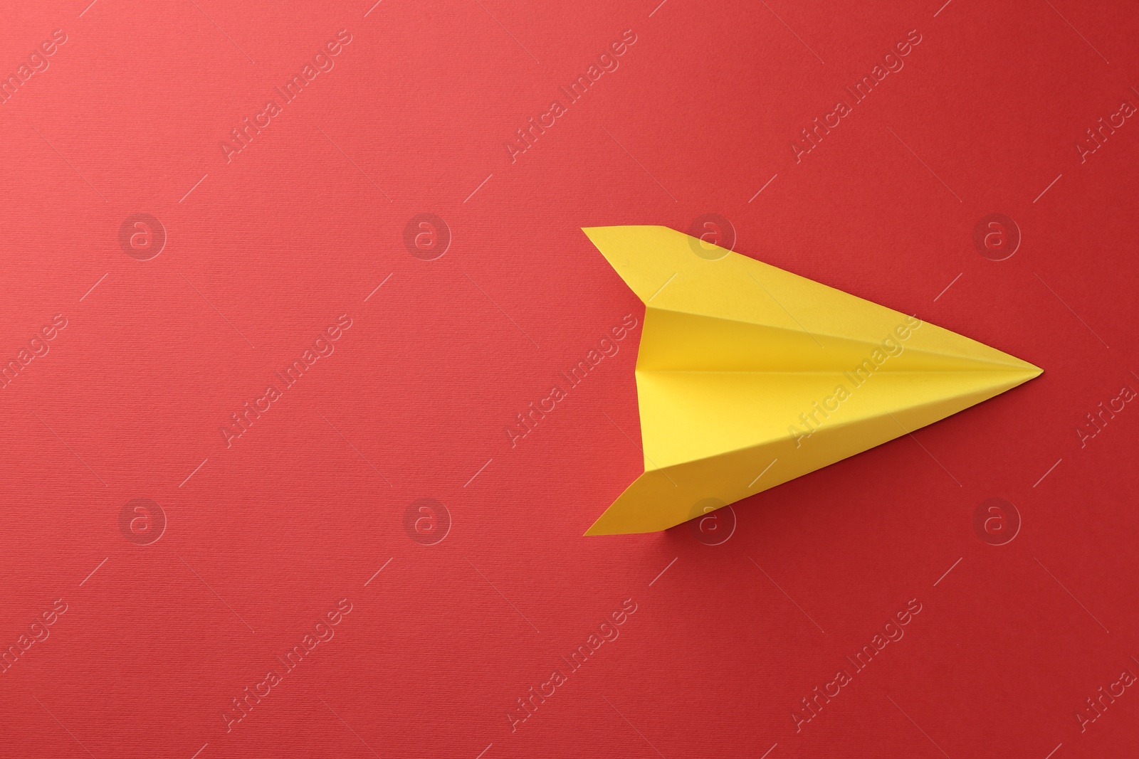 Photo of One handmade yellow paper plane on red background, top view. Space for text