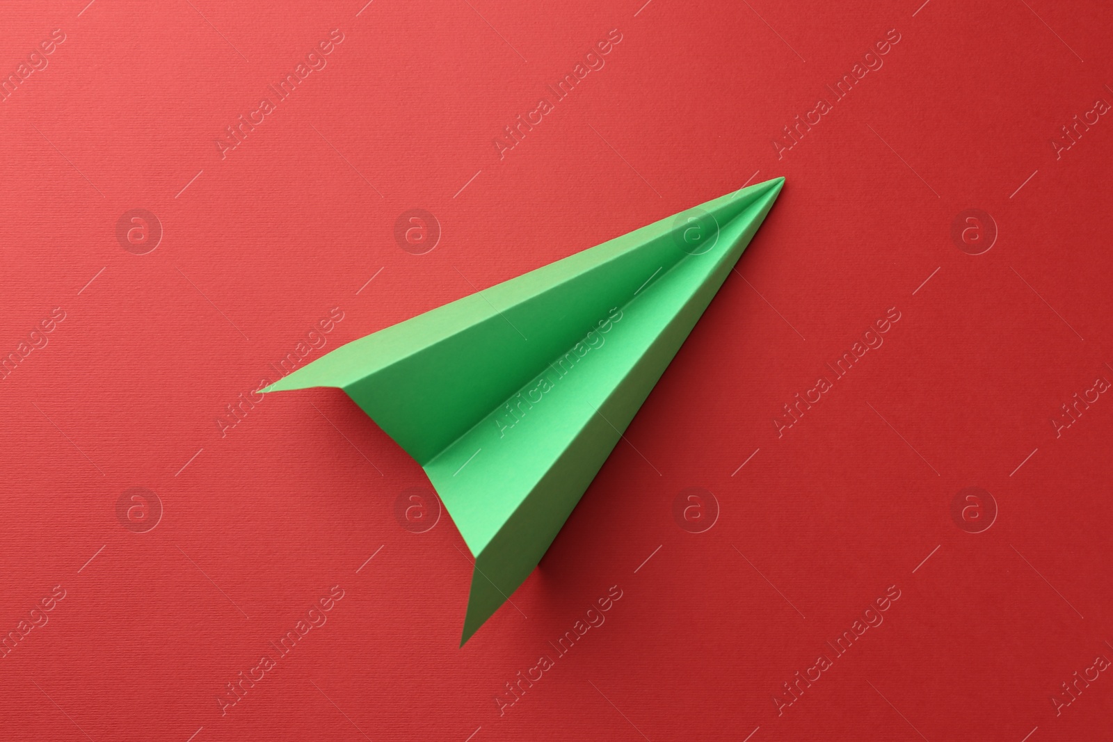 Photo of One handmade green paper plane on red background, top view