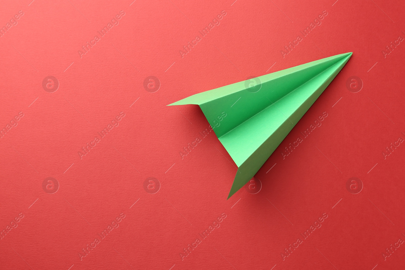 Photo of One handmade green paper plane on red background, top view. Space for text