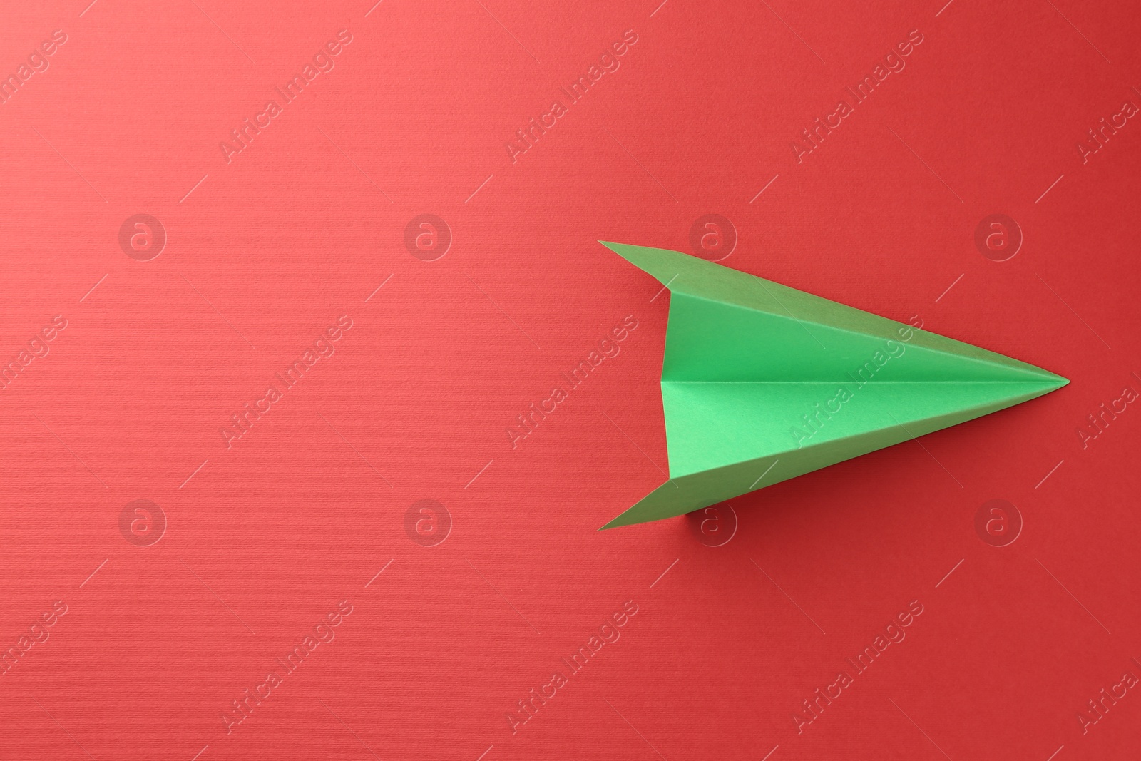 Photo of One handmade green paper plane on red background, top view. Space for text