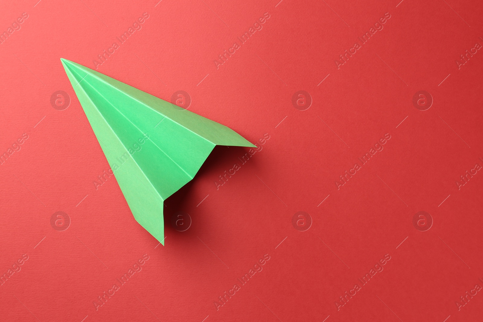 Photo of One handmade green paper plane on red background, top view. Space for text