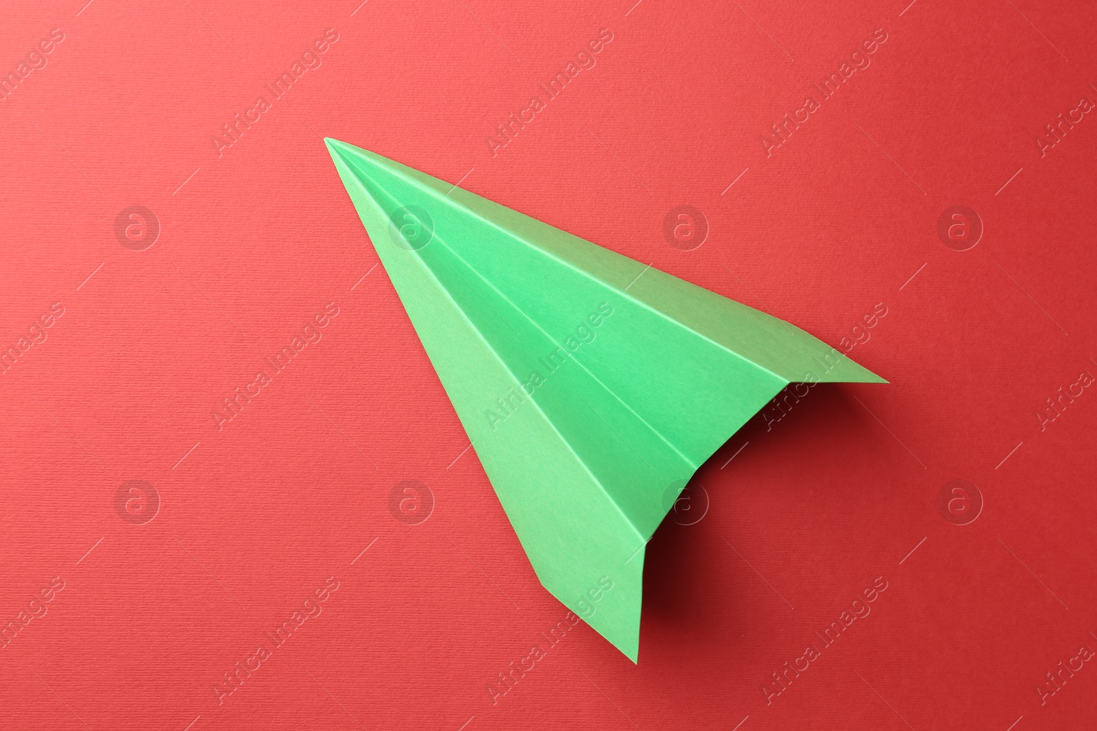 Photo of One handmade green paper plane on red background, top view