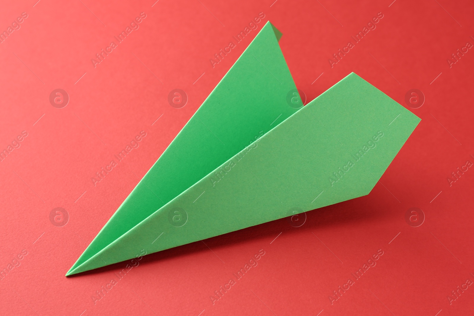 Photo of One handmade green paper plane on red background