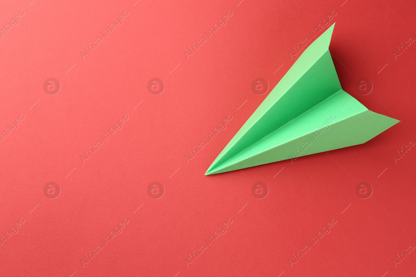 Photo of One handmade green paper plane on red background, top view. Space for text