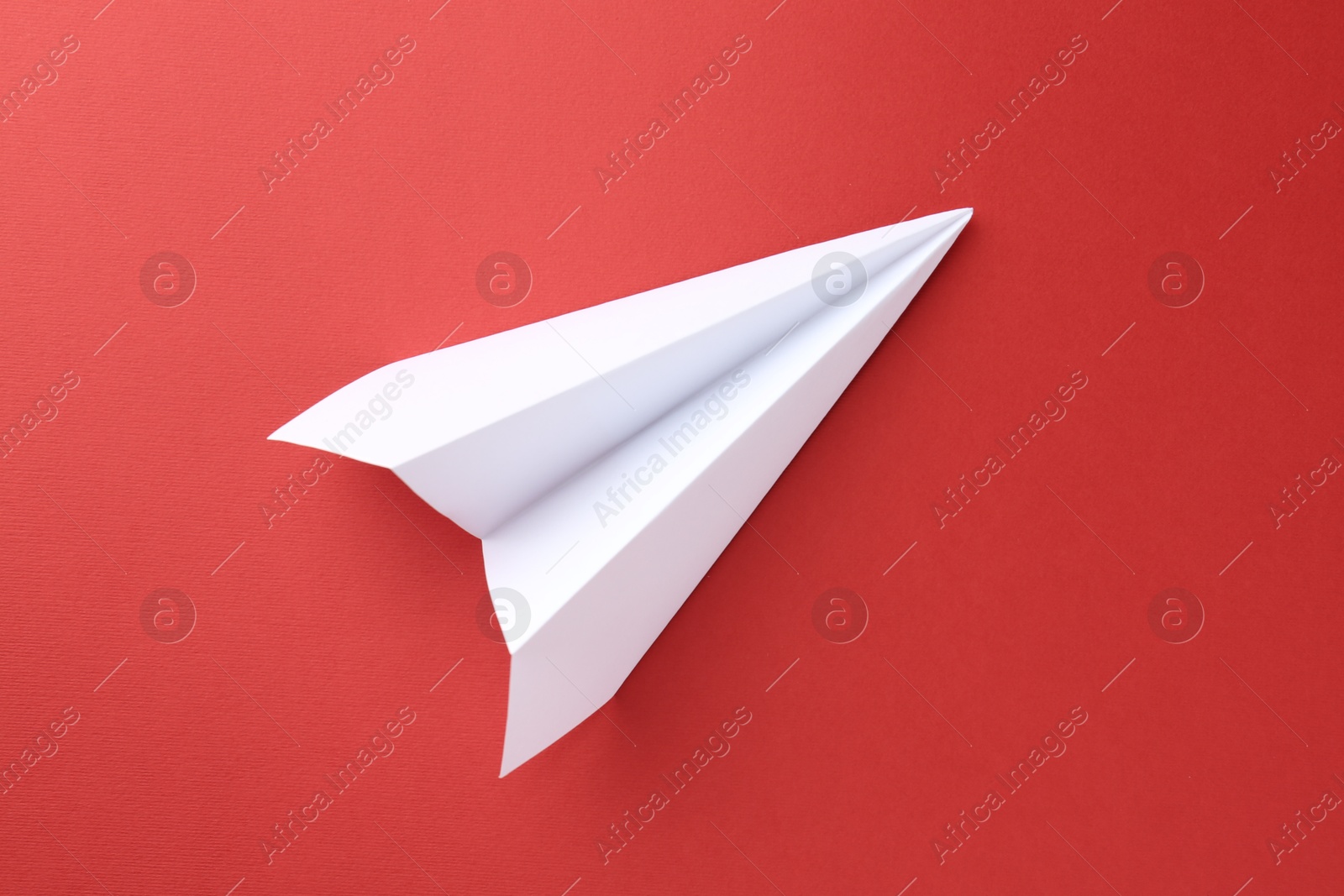 Photo of One handmade paper plane on red background, top view