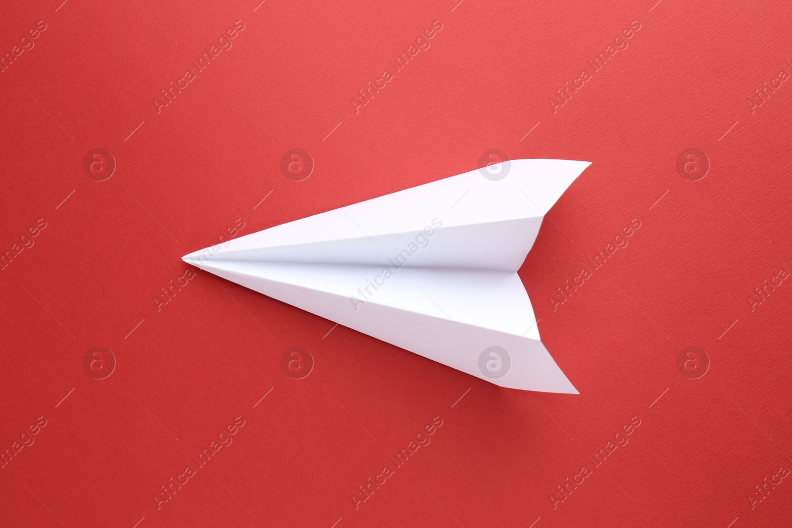 Photo of One handmade paper plane on red background, top view