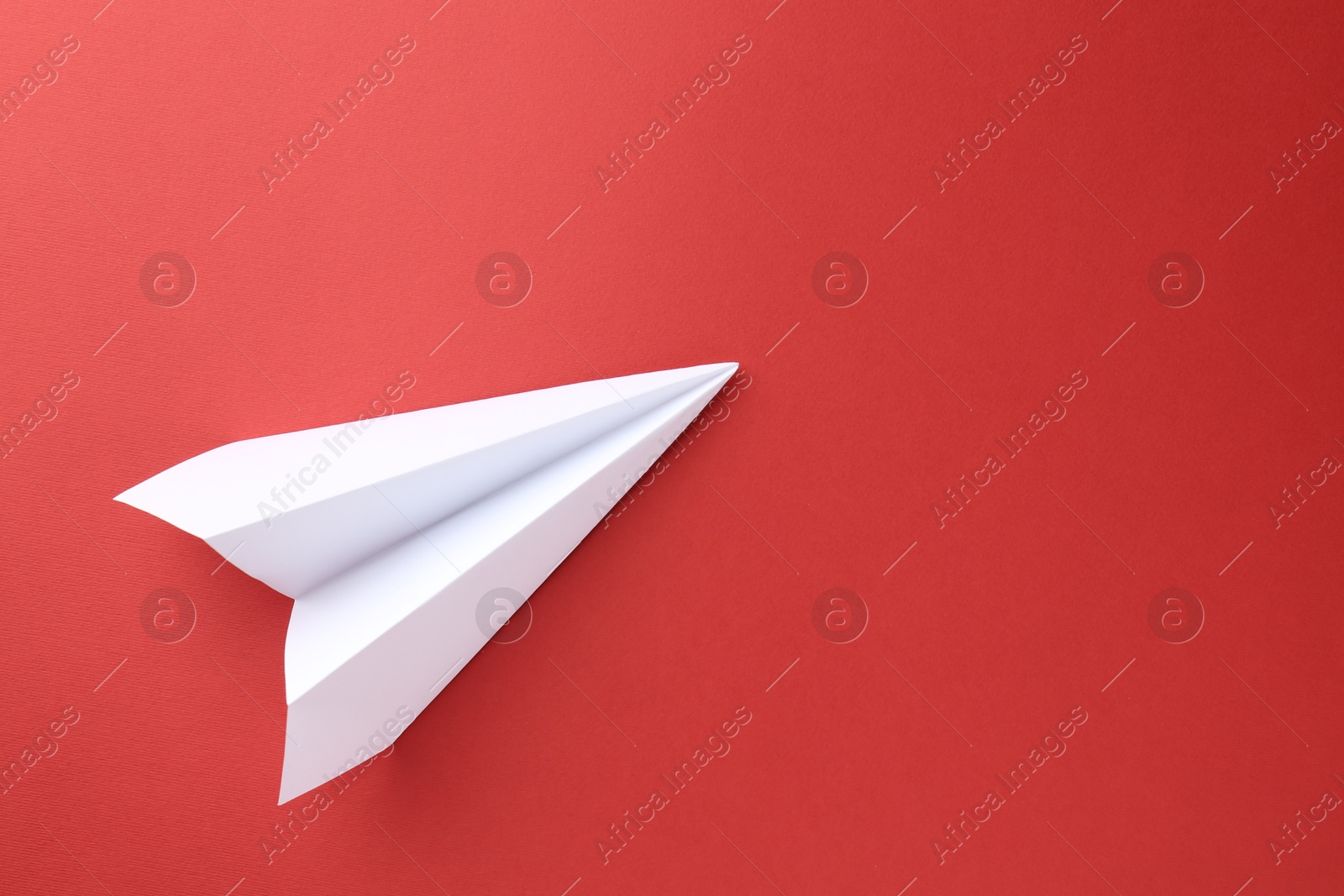 Photo of One handmade paper plane on red background, top view. Space for text