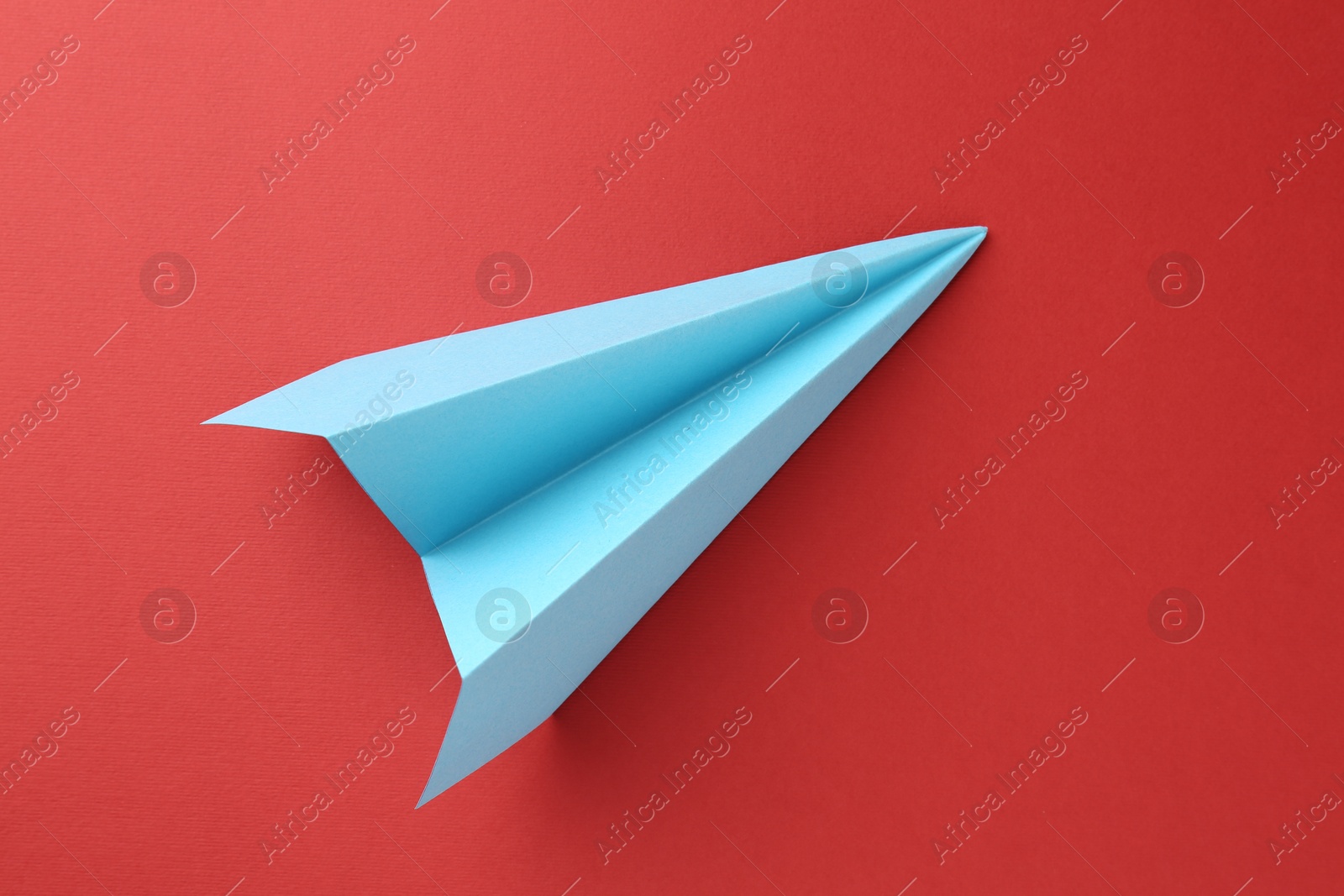 Photo of One handmade light blue paper plane on red background, top view