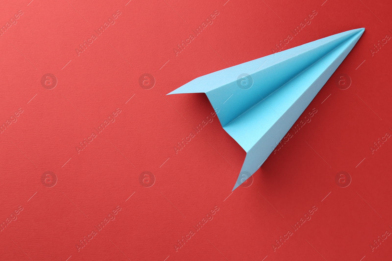 Photo of One handmade light blue paper plane on red background, top view. Space for text