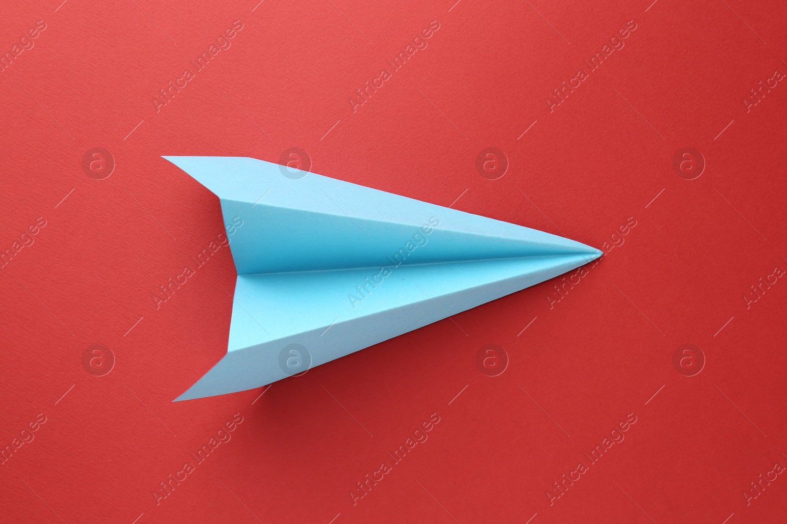 Photo of One handmade light blue paper plane on red background, top view