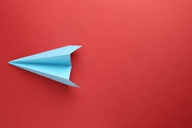 Photo of One handmade light blue paper plane on red background, top view. Space for text