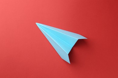 Photo of One handmade light blue paper plane on red background, top view