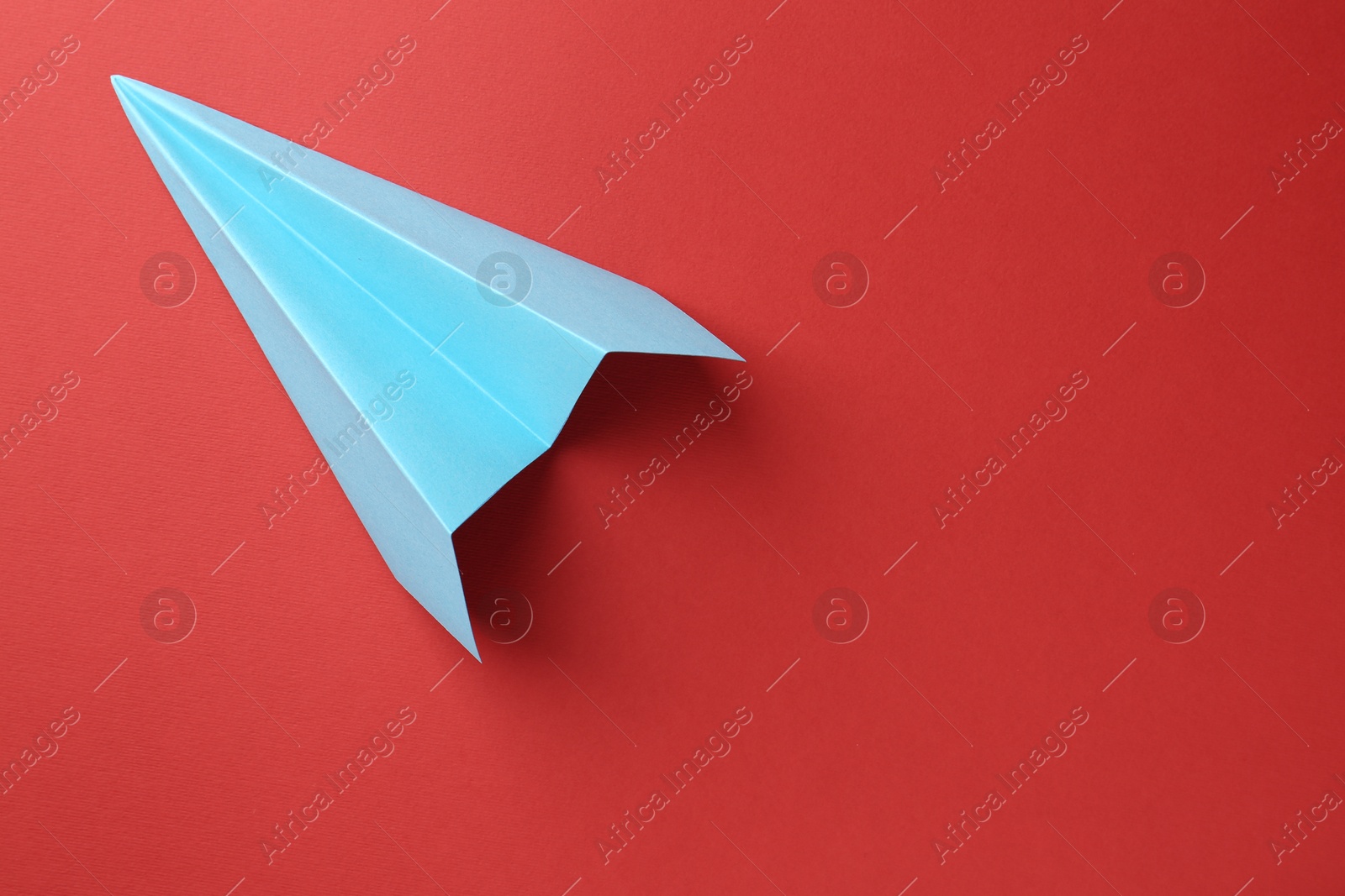 Photo of One handmade light blue paper plane on red background, top view. Space for text