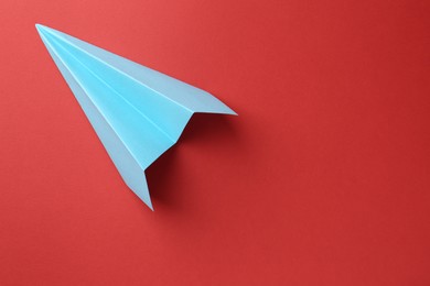 Photo of One handmade light blue paper plane on red background, top view. Space for text