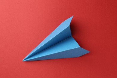 Photo of One handmade light blue paper plane on red background, top view