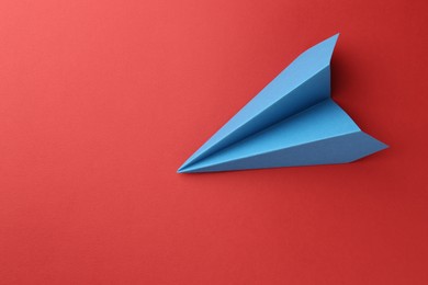 One handmade light blue paper plane on red background, top view. Space for text