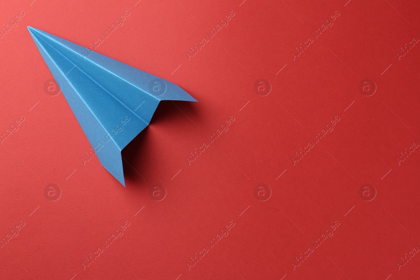 Photo of One handmade light blue paper plane on red background, top view. Space for text