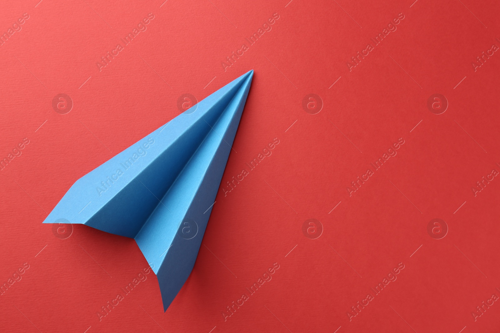 Photo of One handmade light blue paper plane on red background, top view. Space for text