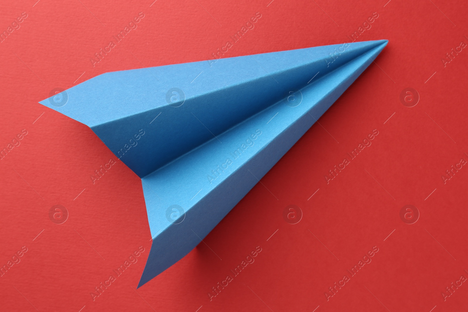 Photo of One handmade light blue paper plane on red background, top view