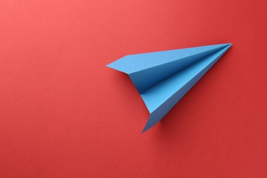 Photo of One handmade light blue paper plane on red background, top view. Space for text