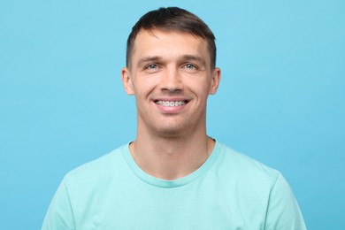 Smiling man with dental braces on light blue background