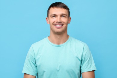 Photo of Smiling man with dental braces on light blue background