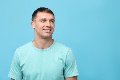 Photo of Smiling man with dental braces on light blue background. Space for text