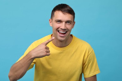 Photo of Happy man pointing at his dental braces on light blue background