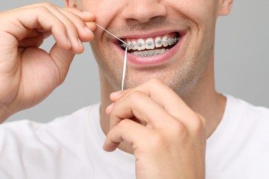 Photo of Man with braces cleaning teeth using dental floss on grey background, closeup