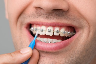 Man with dental braces cleaning teeth using interdental brush on grey background, closeup