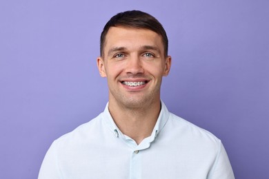 Photo of Smiling man with dental braces on violet background