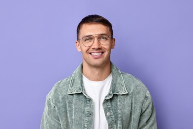 Smiling man with dental braces on violet background